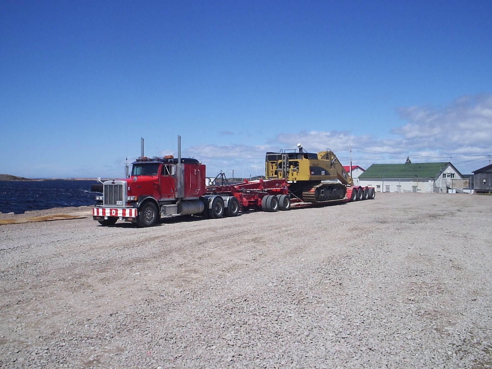 Peterbilt SM Plus tirant une excavatrice sur fardier au bord du fleuve