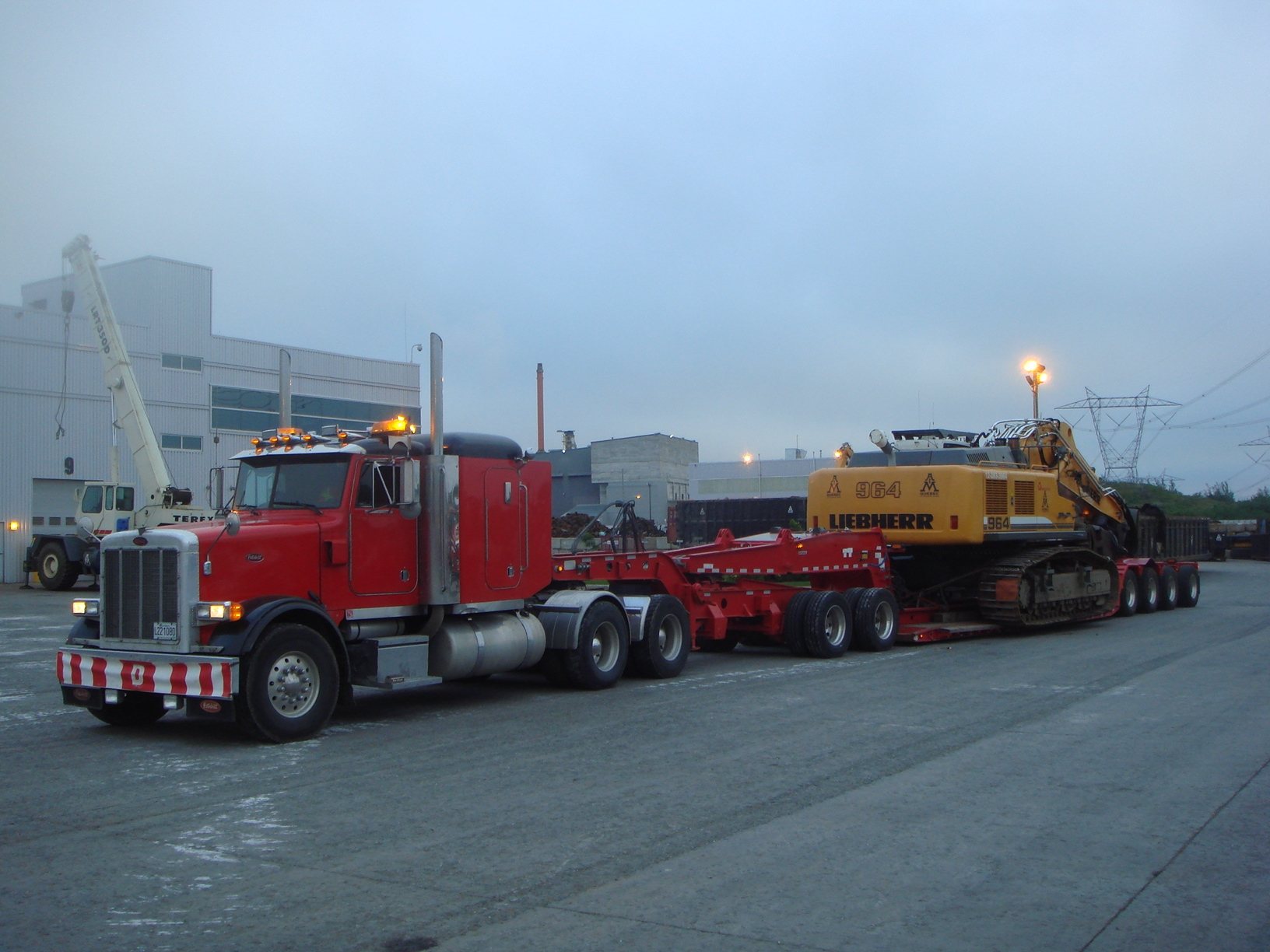 Transport d'une pelle Liebherr sur fardier devant une usine